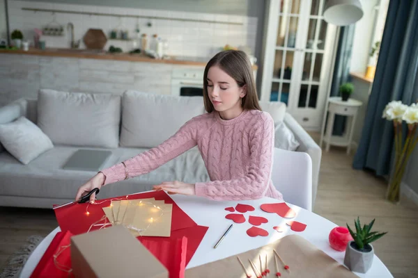 Gadis berambut gelap dalam kemeja merah muda tampak sibuk dengan mempersiapkan hadiah — Stok Foto