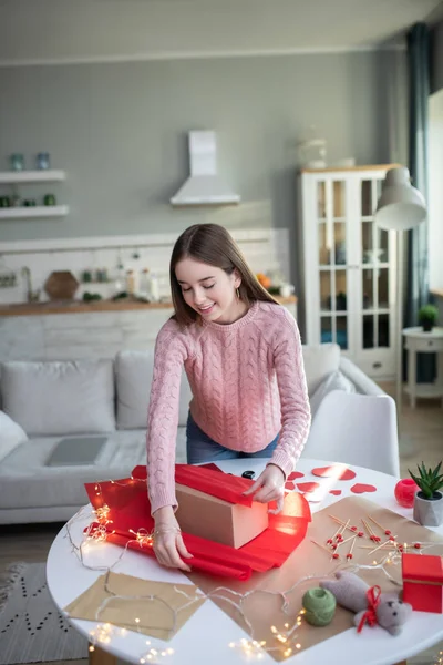 Donkerharig met rood papieren meisje in een roze shirt over een geschenkdoos — Stockfoto
