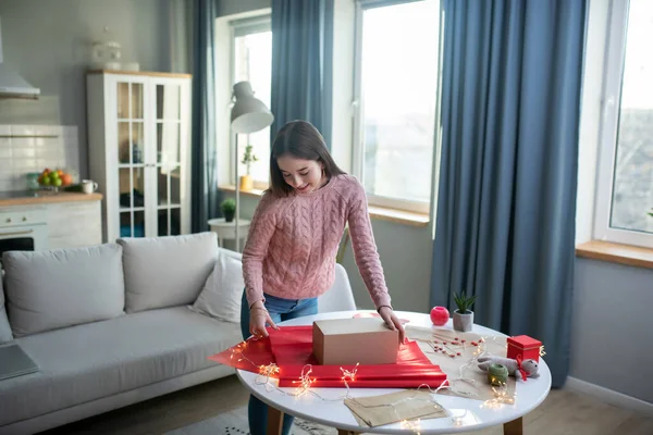 Dark-haired girl in a pink shirt making a gift box — Stock Photo, Image