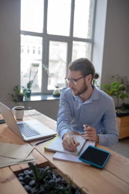 Elinde kalemle dizüstü bilgisayara bakan başarılı bir adam..