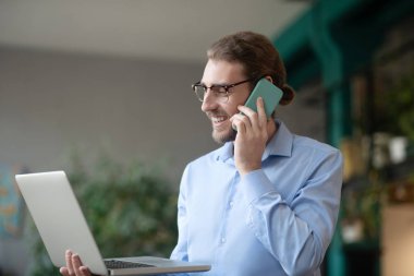 Bilgisayarlı başarılı genç adam akıllı telefondan konuşuyor..