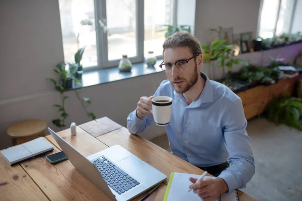 Молодой человек сидит за столом в офисе и пьет кофе. . — стоковое фото