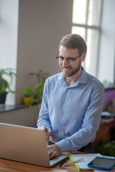 Jovem homem alegre trabalhando em um laptop em um escritório . — Fotografia de Stock