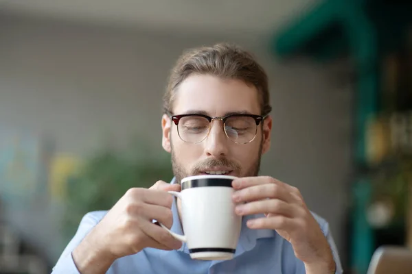 戴眼镜的年轻人微笑着看着一杯咖啡. — 图库照片