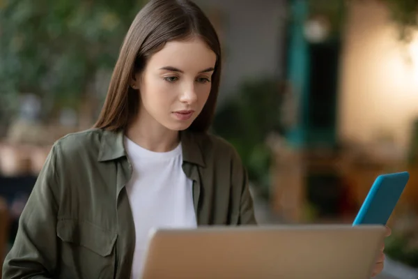 Trött flicka som arbetar på en bärbar dator, tittar på en tablett. — Stockfoto