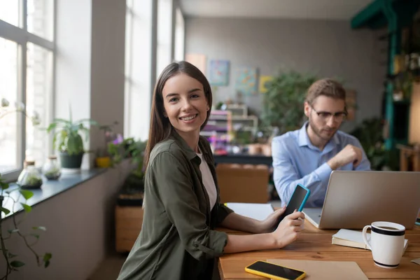 Glimlachend meisje met tablet, naast collega op laptop. — Stockfoto