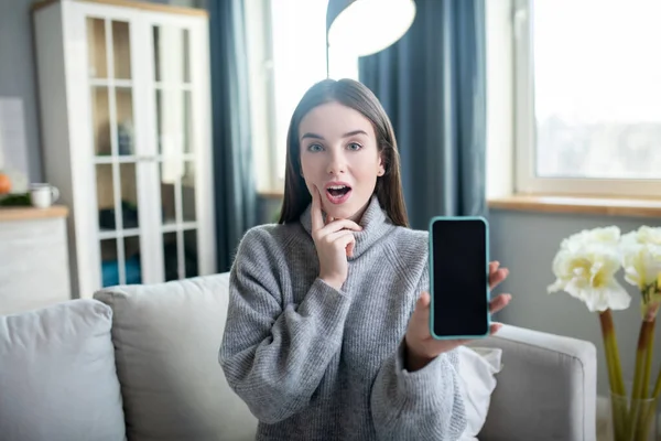 Chica joven en un suéter gris mostrando su teléfono inteligente — Foto de Stock