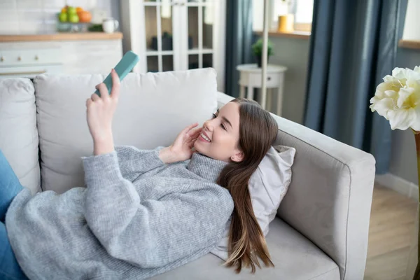 Chica joven en un suéter gris teniendo una llamada por video — Foto de Stock