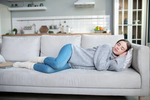 Chica joven en un suéter gris tomando una siesta en un sofá — Foto de Stock