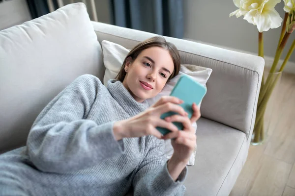 Chica joven en un suéter gris sosteniendo un teléfono inteligente — Foto de Stock