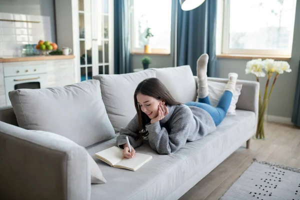 Молода дівчина в сірому светрі лежить на дивані — стокове фото