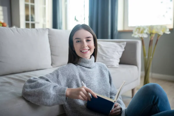 Chica joven en un suéter gris sentada en el suelo y sonriendo — Foto de Stock