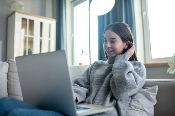 Chica joven en un suéter gris teniendo un videochat — Foto de Stock