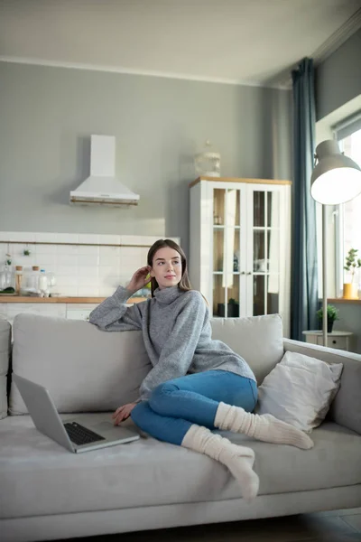 Mladá dívka v šedém svetru vypadá zamyšleně — Stock fotografie