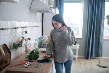 Dark-haired girl in a grey sweater searching for something in her gadget