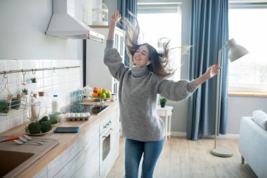 Dark-haired girl in a grey sweater having fun at home