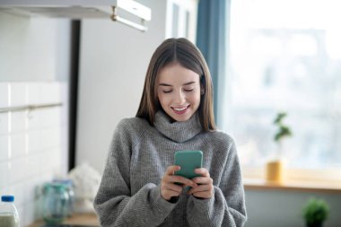 Dark-haired girl in a grey sweater typing a message