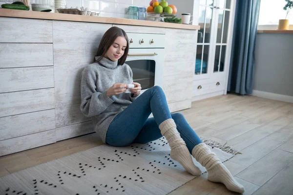 Dark-haired girl in a grey sweater opening a box wirh wireless earphones — Stok fotoğraf