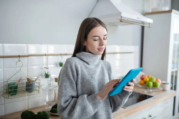 Fille aux cheveux foncés dans un pull gris lisant quelque chose sur sa tablette — Photo