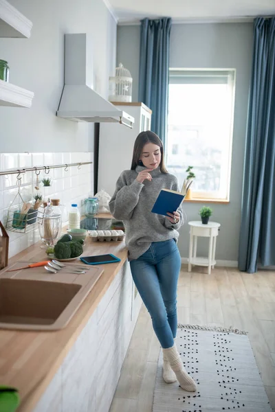 Chica de pelo oscuro en un suéter gris leyendo y buscando involucrado — Foto de Stock