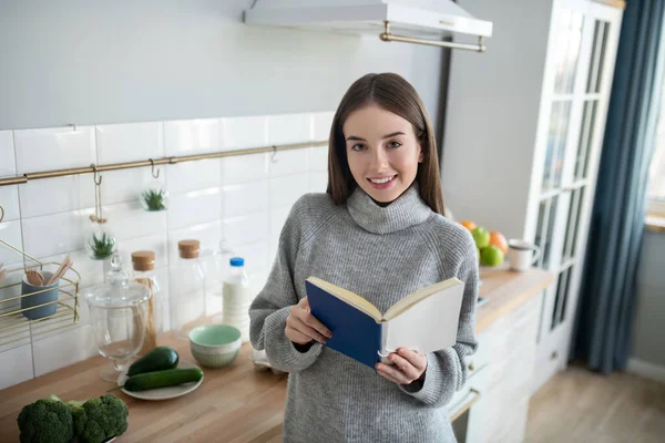 Chica de pelo oscuro en un suéter gris sosteniendo un libro — Foto de Stock