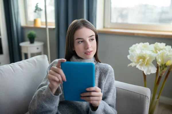 Chica de pelo oscuro en un suéter gris con una tableta mirando reflexivo — Foto de Stock