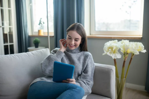 Chica de pelo oscuro en un suéter gris leyendo algo en línea — Foto de Stock