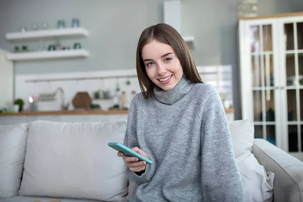 Chica de pelo oscuro en un suéter gris sonriendo felizmente — Foto de Stock