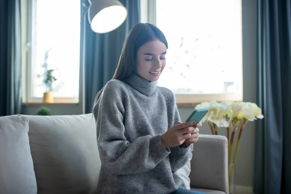 Dark-haired girl in a grey sweater spending time online — Stok fotoğraf