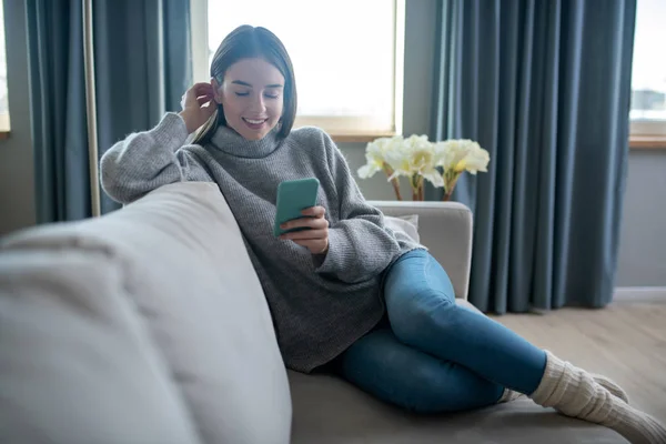 Chica de pelo oscuro en un suéter gris leyendo un mensaje — Foto de Stock