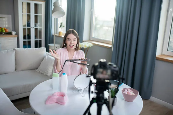 Sonriente chica bonita en una camisa rosa sosteniendo un rizador — Foto de Stock