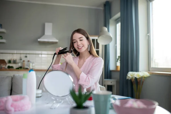 Sonriente chica bonita en una camisa rosa rizando su cabello — Foto de Stock