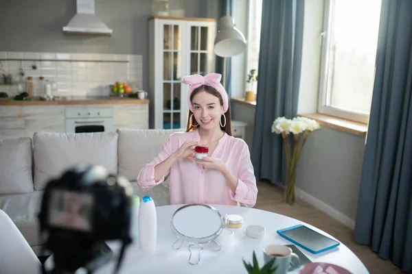 Sonriente chica bonita en una diadema rosa demostrando nueva crema facial — Foto de Stock