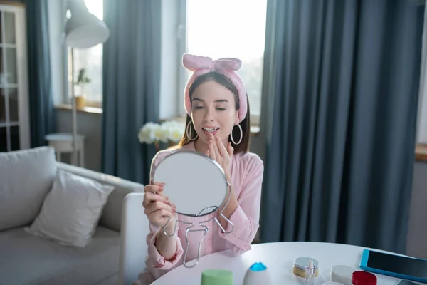 Sonriente chica bonita en una diadema rosa mirando en el espejo — Foto de Stock