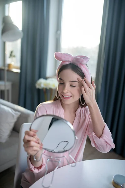 Χαμογελώντας όμορφο κορίτσι σε ένα ροζ κεφαλόδεσμο κοιτάζοντας τον εαυτό της — Φωτογραφία Αρχείου