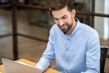 Young bearded man sitting at the laptop and smiling