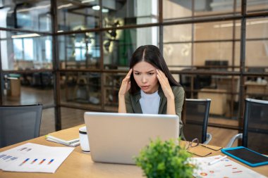 Long-haired brunette asian girl working in the office and having a headache