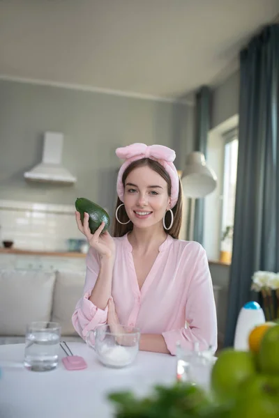 Улыбающаяся красивая девушка в розовом повязке с авокадо в руке — стоковое фото