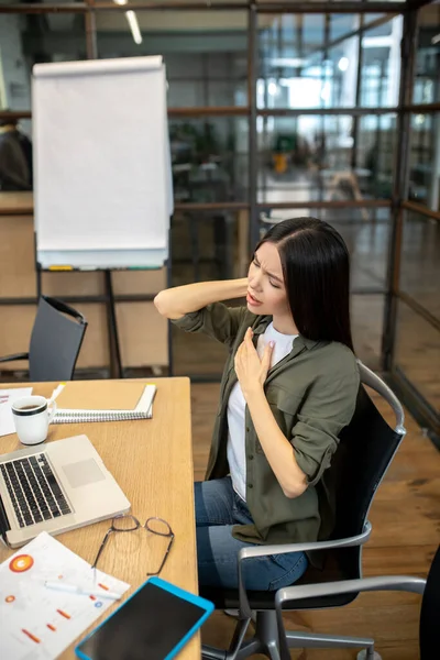 Hosszú hajú barna hajú ázsiai lány dolgozik az irodában, és fáj a nyaka. — Stock Fotó