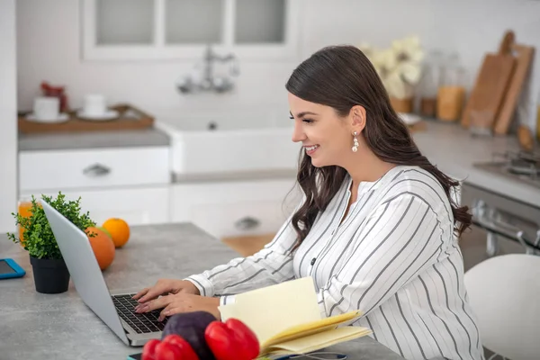 Mujer de pelo largo con una blusa a rayas sentada en la mesa y mirando involucrada — Foto de Stock