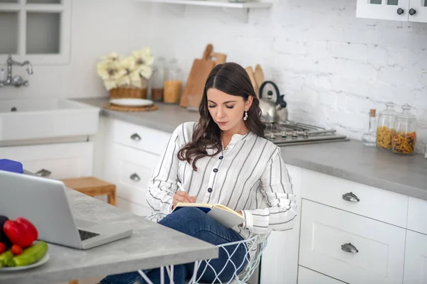 Mujer de pelo largo en blusa a rayas sentada a la mesa y leyendo — Foto de Stock