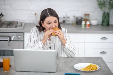 Dark-haired woman in a striped blouse eating a burger