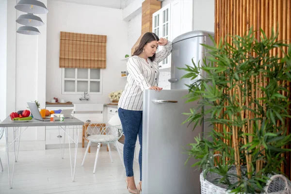 Dark-haired woman in a striped blouse opening the fridge — Stockfoto