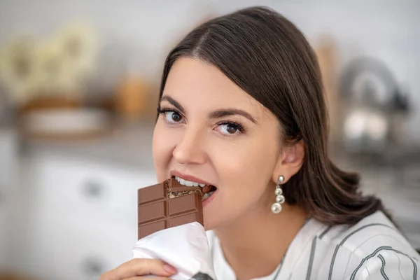 Dunkelhaarige Frau in gestreifter Bluse, die Schokolade isst — Stockfoto