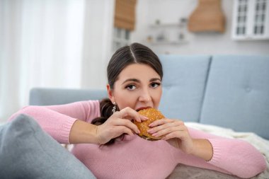 Full-figured young woman in a pink shirt eating a burger