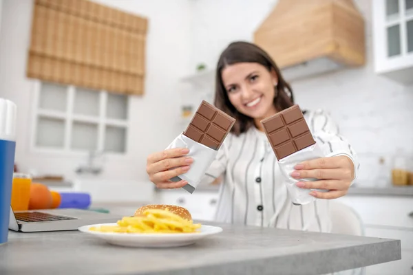 Dark-haired woman in a striped blouse holding two bars of chocolate — 스톡 사진