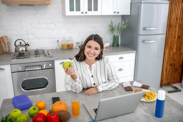 Темноволосая женщина в полосатой блузке сидит за столом с овощами — стоковое фото