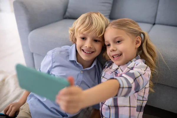 Niño y niña sentados en el suelo, tomando selfie — Foto de Stock