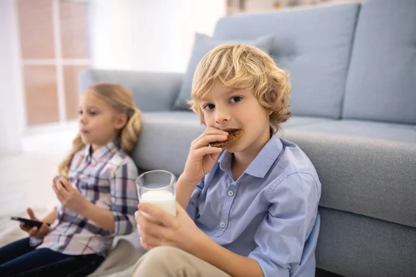 Menino mordendo biscoito e bebendo leite, menina mudando canais — Fotografia de Stock