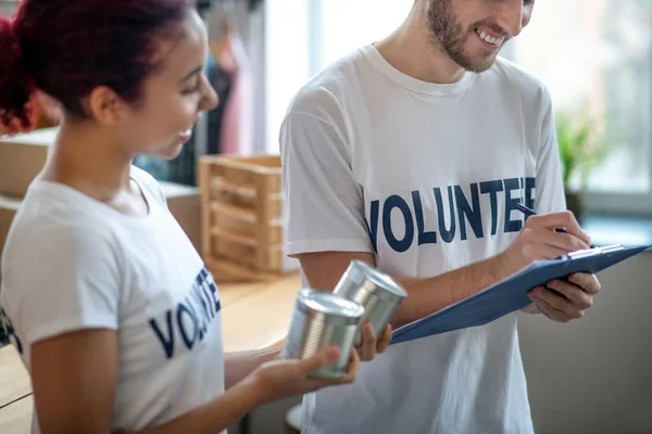 Ung man som skriver produkter, flicka som håller konserverad mat. — Stockfoto